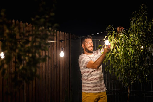 A man touching a light bulb outside at night.