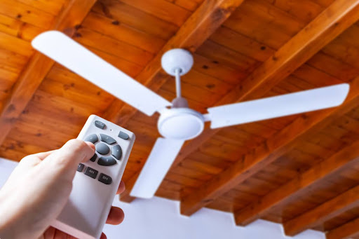 Hand pressing remote pointed towards white ceiling fan.