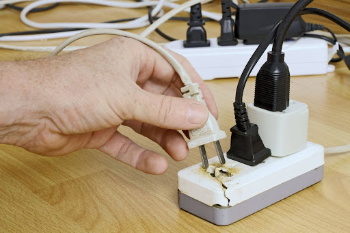 Hand taking out plug from singed extension cord outlet.