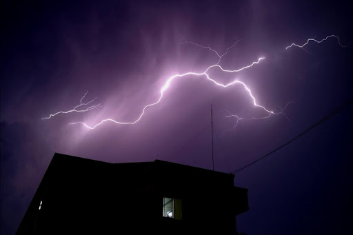 The exterior of a house at night with lightning flashing in the sky.
