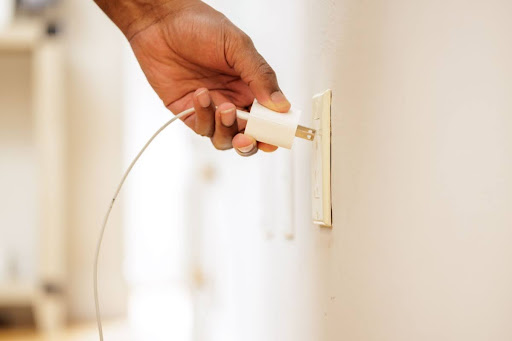 A hand plugging a charger into an outlet on a wall.